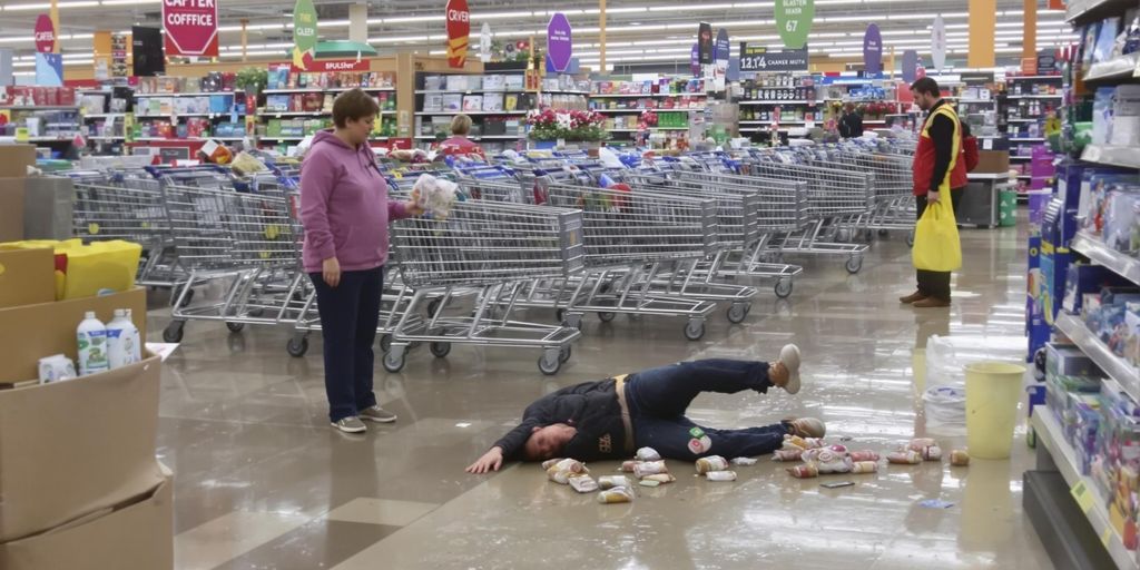 Person slipping on wet grocery store floor with spilled groceries.