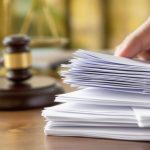 Hand holding documents with gavel and scales nearby.