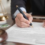 Person filling legal documents with gavel and justice scale