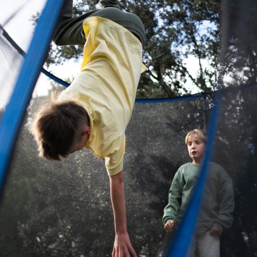 Boy upside down doing a backflip on a trampoline while his friend watches him