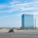 Motorcyclist on road, legal firm in background.