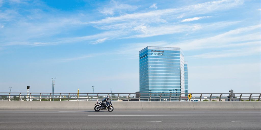 Motorcyclist on road, legal firm in background.